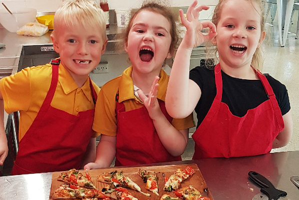 Three children making happy faces over slices of pizza