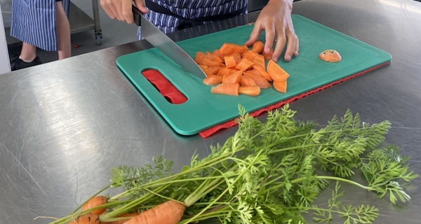 Carrots being chopped on a green board, on a stainless steel bench