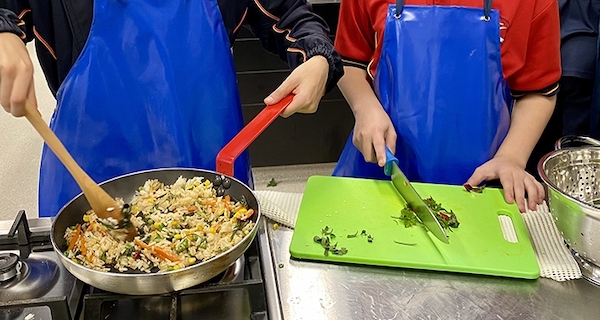 Hands chopping on bright boards; torsos in blue aprons visible