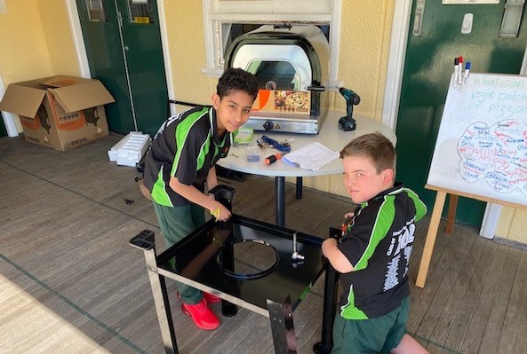 Two children constructing portable pizza ovens