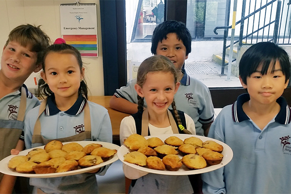 Five children in kitchen, two at front holding plates of muffins